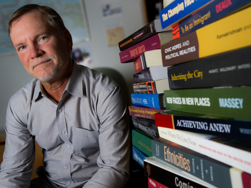 A professor sitting by stacks of books on desk A professor sitting by stacks of books on desk